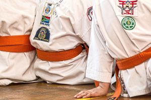 Kids sitting on the floor in kimonos with orange belts as beginner Karate students