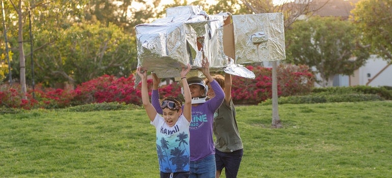 Three kids are running around carrying a big old airplane toy.