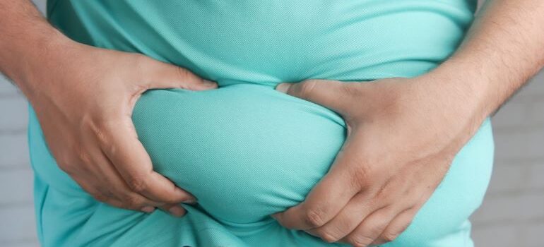 a man holding his belly fat while thinking to get a six-pack in 5 simple steps