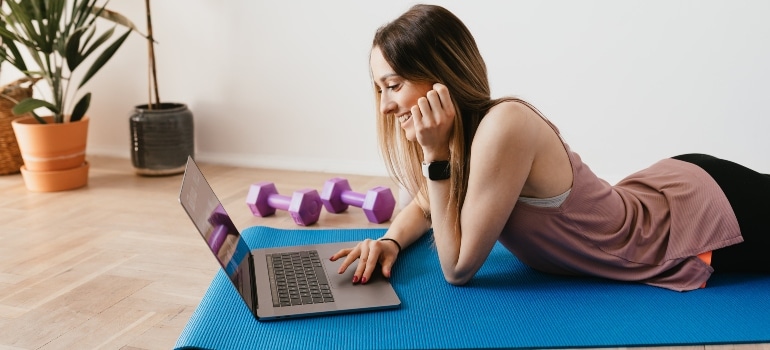 A woman laying on a yoga mat and reading about the power of fitness over anxiety and depression on her laptop