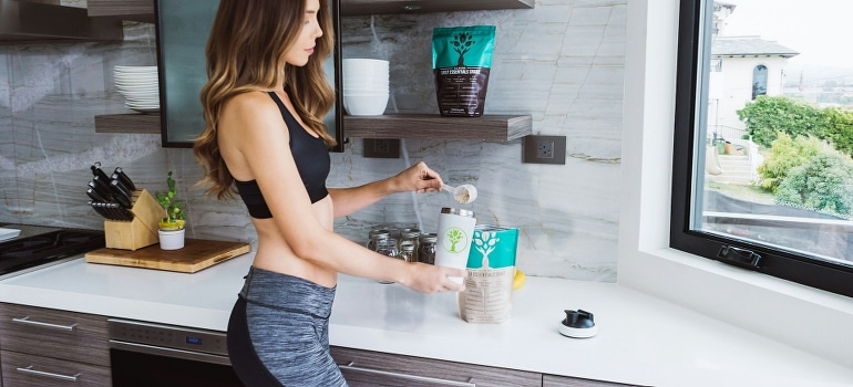 A woman in a kitchen using protein powder.