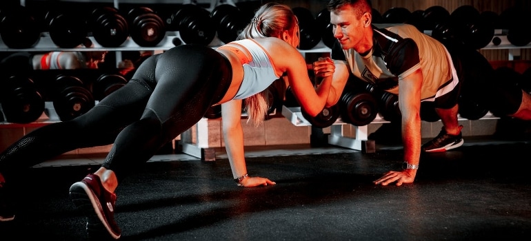 A couple holding their hands while doing push-ups.