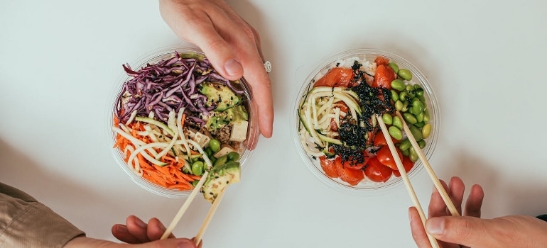 Two people holding salad bowls and chopsticks.