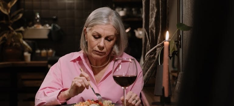 An older woman eating dinner and drinking a glass of wine.