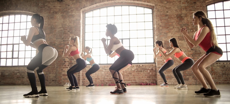 A group performing a squat with proper form, keeping a neutral spine and knees aligned with toes to avoid common errors in resistance training