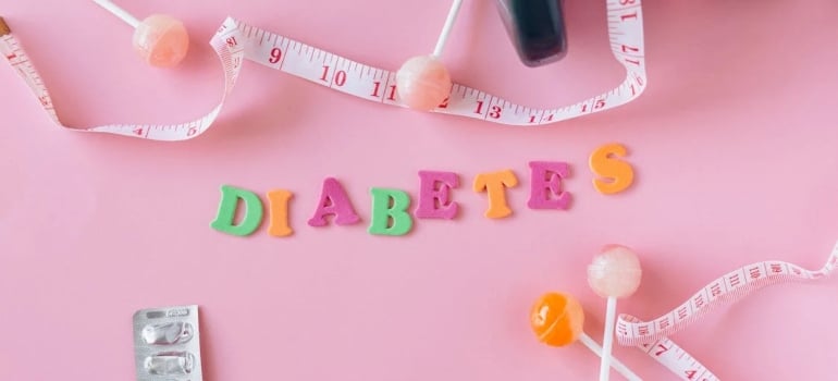 Lollipops, meter and medicaments on a pink background around letters creating a word diabetes