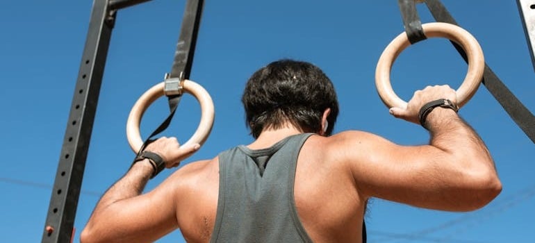 A man in a gray tank top holding on gymnastic rings