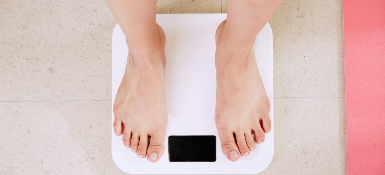 Person stepping on a scale after not eating the 7 foods to avoid for weight loss