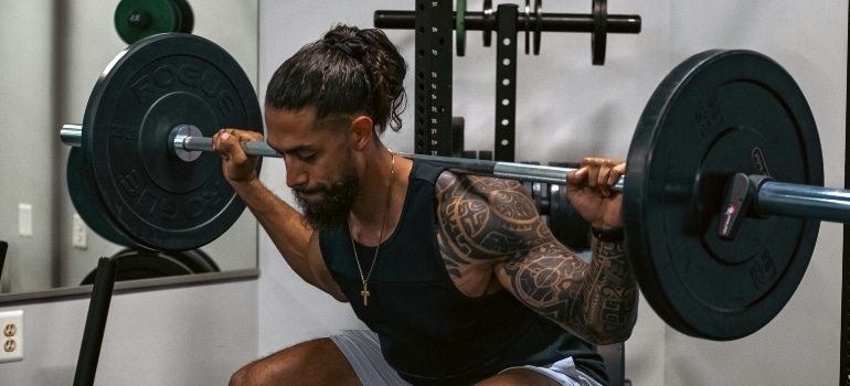 A tattooed man is lifting a barbell in Dubai's gym.