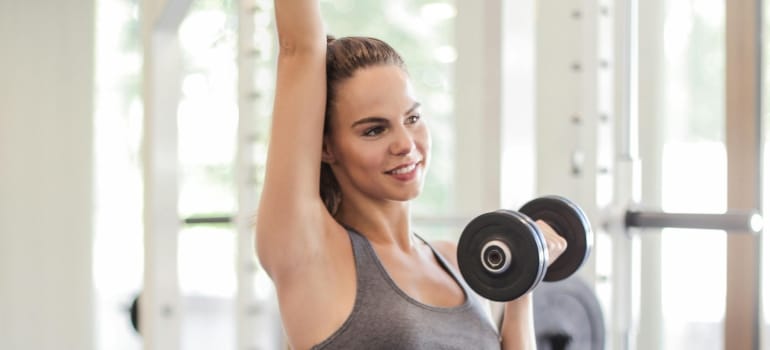 A smiling woman is using dumbbells.