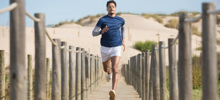 Man jogging along a wooden boardwalk by the beach, balancing higher intensity runs with low-impact cardio alternatives for days when you’re feeling sore.
