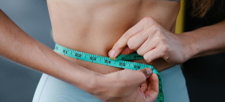 Woman measuring her waist, showing progress from fat loss workouts in humid conditions