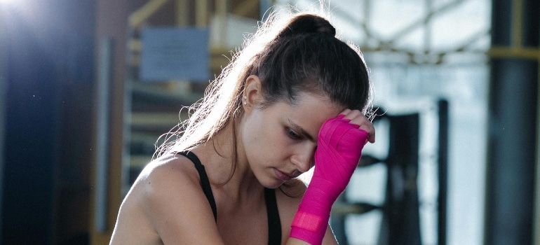 Tired woman in gym wiping sweat, showing fatigue caused by humid workout conditions
