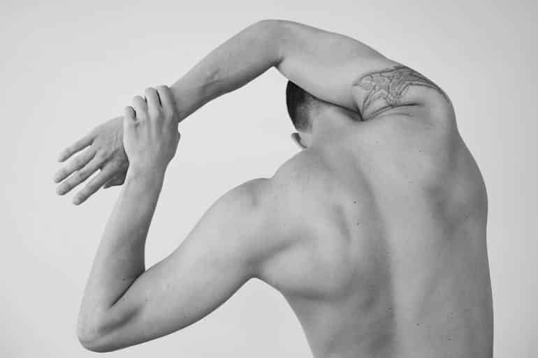 Back view of a shirtless man stretching his arms overhead during a post-workout warm-down.