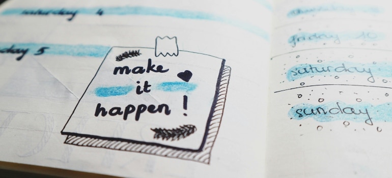 Open planner with doodles and blue highlights, featuring a note that says “make it happen!” next to weekend plans.