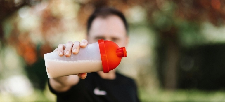 A person holding a shake bottle, eating avoid the hidden cost of under-eating while training in Dubai.