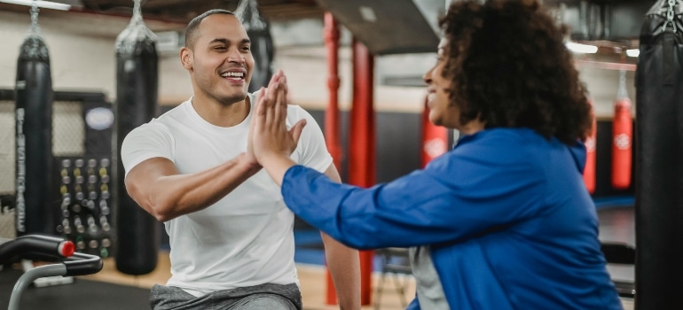 Personal trainer and client high-fiving in a fitness studio, showing is hiring a personal trainer in Dubai worth it in 2026.