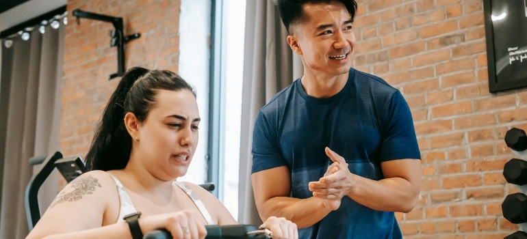 Personal trainer encouraging a woman during a cardio workout in a bright gym with brick walls.