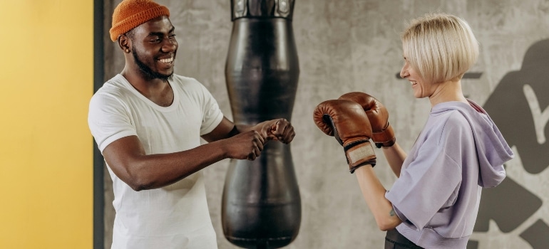 Trainer and woman in boxing gloves smiling during a gym session, showing is hiring a personal trainer in Dubai worth it in 2026.